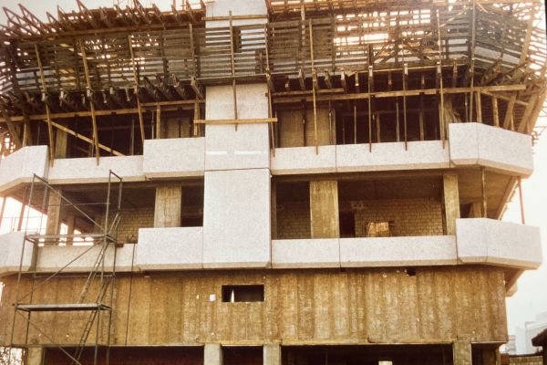 Das Hotel Seelust während der Bauarbeiten am mehrstöckigen Ausbau mit Sichtbeton, Gerüsten und Holzbalken im obersten Stockwerk. Die mittleren Stockwerke haben große offene Fensterflächen, und Baumaterialien sind sichtbar.