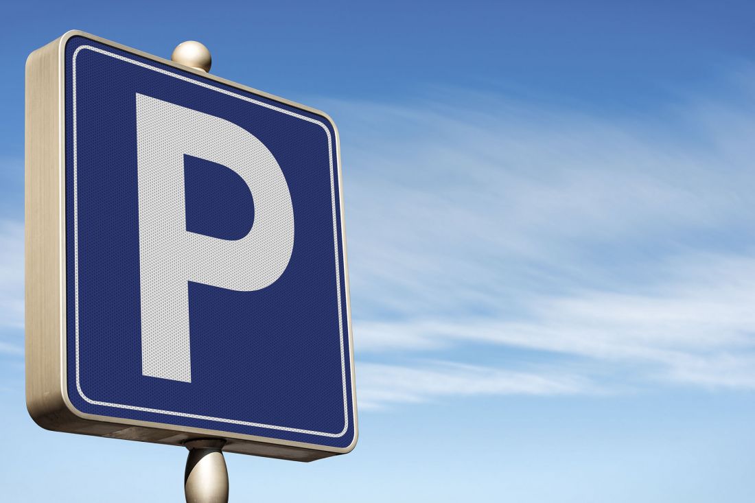 Ein blaues Parkplatzschild mit einem großen weißen P darauf steht vor einem klaren blauen Himmel mit Wolkenfetzen.